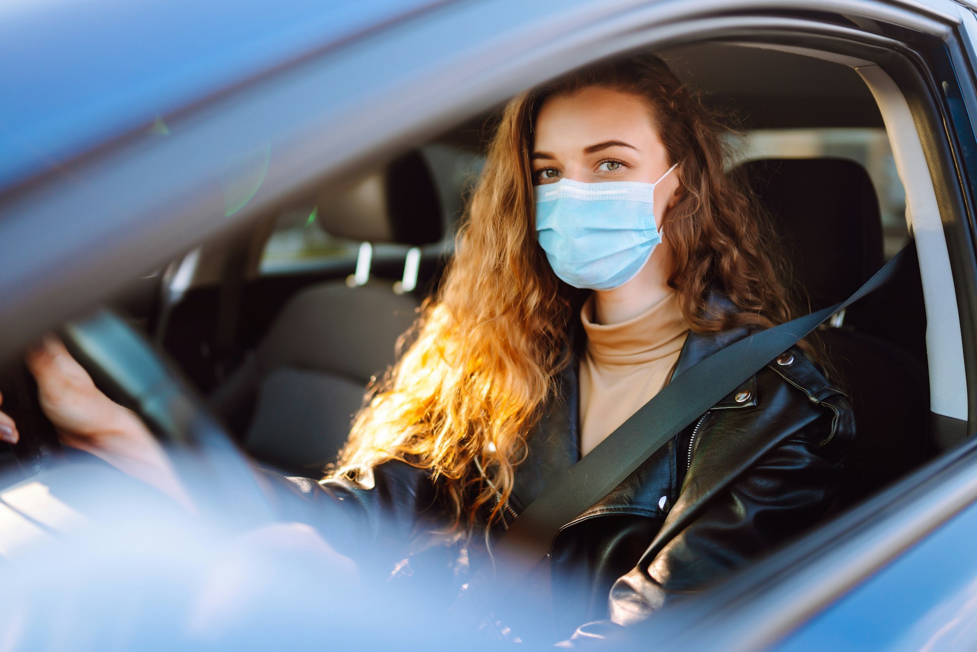 Young woman driving a car wearing on a medical mask during an epidemic. Transport isolation. Covid.